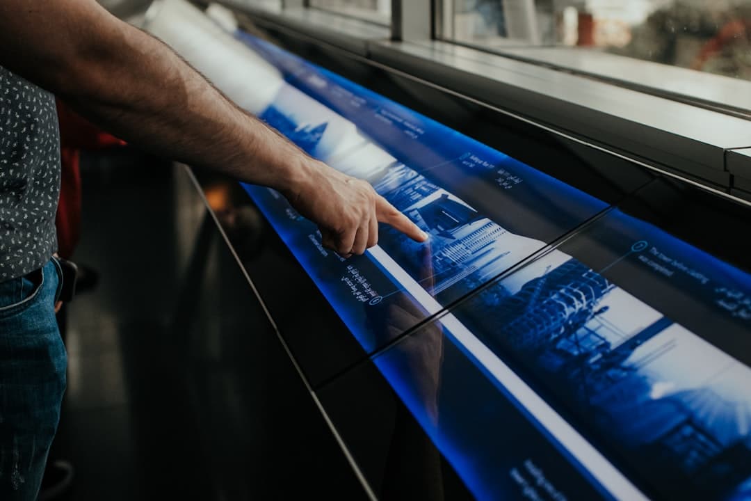 A person points at a futuristic, interactive touchscreen display with blue graphics and text.