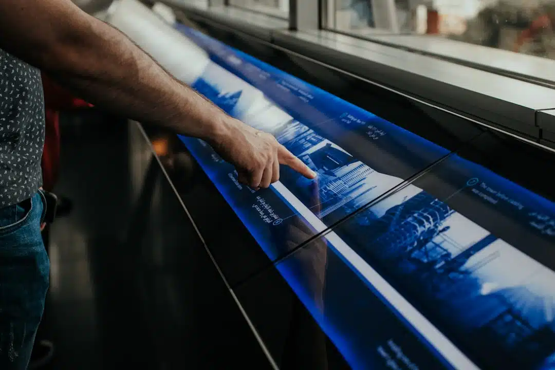 A person points at a futuristic, interactive touchscreen display with blue graphics and text.
