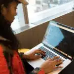 Person typing code on a laptop while sitting indoors near a large window.