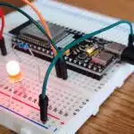 Close-up of a breadboard with an LED, wires, and a microcontroller connected, all placed on a wooden surface.