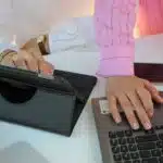 Two people working at a desk with a tablet, laptop, smartphone, and a cup of tea.