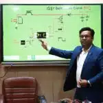 Man in suit pointing to a digital IGBT gate driver circuit diagram on a screen in a classroom or lab.