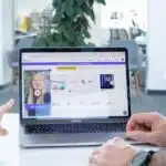 Two people video conferencing on a laptop in a modern office setting.