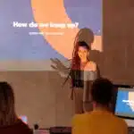 Woman presenting a slideshow titled "How do we keep up? Constant Evolution" to two seated people.