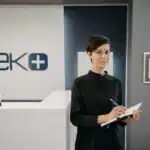 A woman in black holds a clipboard and pen at a modern dental clinic reception area.