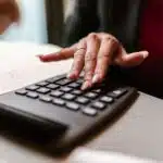 A person using a calculator with one hand and an open notebook nearby on the desk.