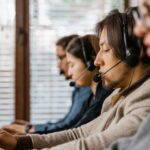 People wearing headsets work on laptops in a row at a call center or customer service office.