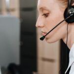 Woman wearing a headset, sitting at a desk and looking at a computer screen in an office setting.
