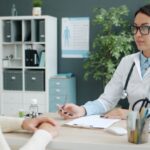 Doctor with stethoscope listens to a patient across a desk in a modern medical office.