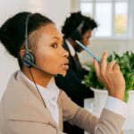 A woman wearing a headset speaks while sitting at an office desk.
